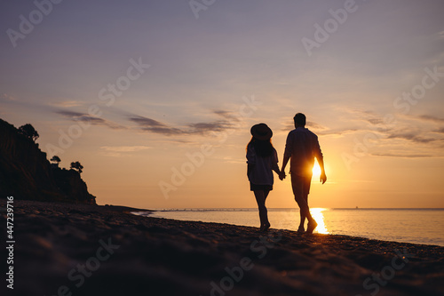 Full body back view silhouette young couple two friends family man woman in casual clothes hold hands walk stroll together at sunrise over sea beach ocean outdoor exotic seaside in summer day evening. © ViDi Studio