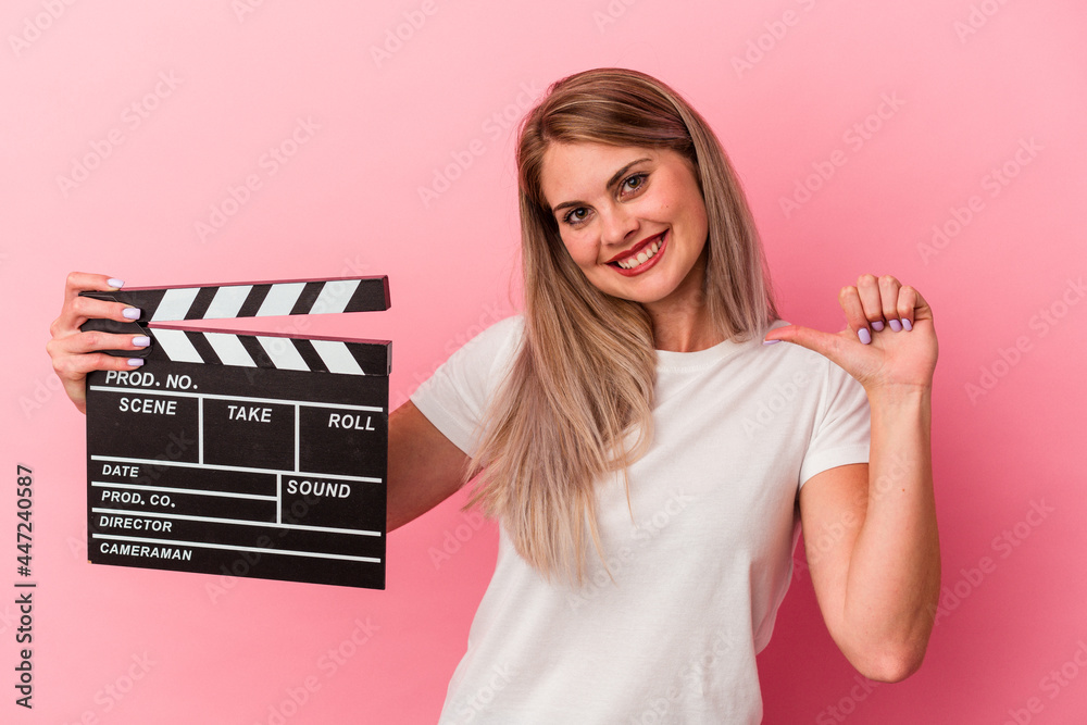 Young Russian woman holding a clapperboard isolated on pink background feels proud and self confident, example to follow.