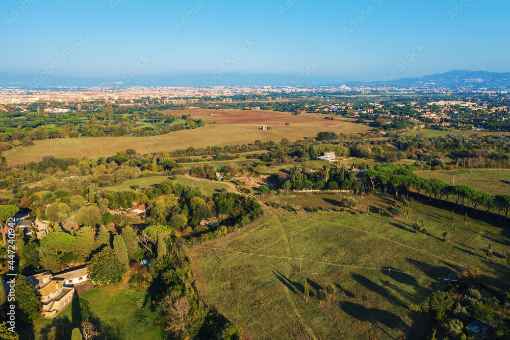 Aerial view of ancient Via Appia Antica with green trees, meadows, houses and pathways in Rome, Italy.