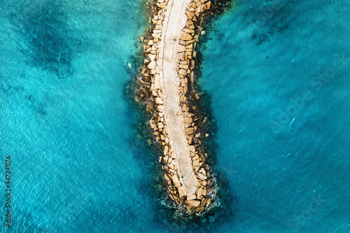 Aerial top down view of stone breakwater in bright blue sea surface.