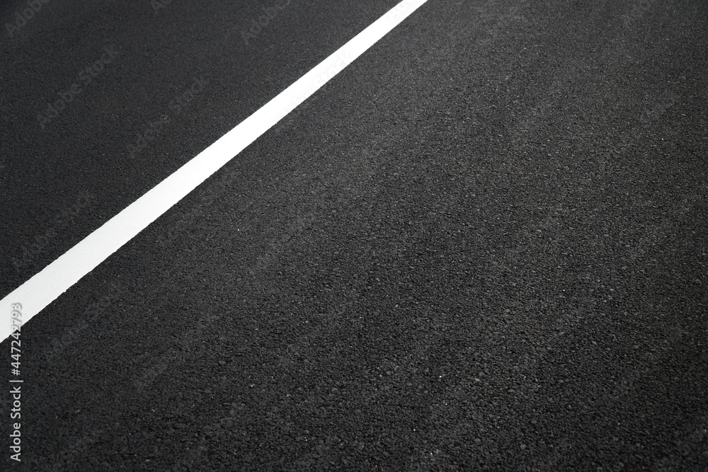 Close up of local black asphalt road surface texture with a separation white line. Selective focus.