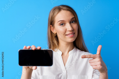 Beautiful young woman showing smartphone screen against blue background photo