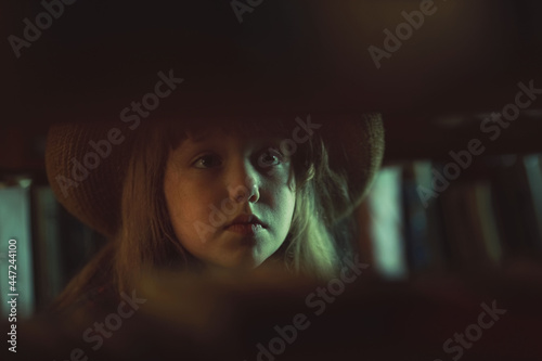 little girl in a drop stands in a retro library and looks at books