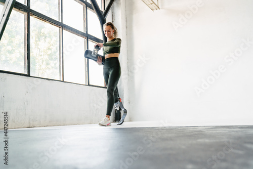 Young sportswoman with prosthesis looking at smarwatch indoors