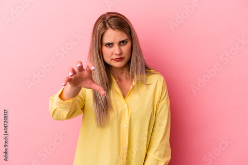 Young russian woman isolated on pink background showing claws imitating a cat, aggressive gesture.