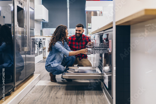Beautiful and happy young couple buying dishwasher in modern appliances store. photo