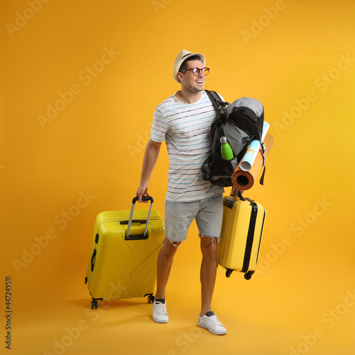 Male tourist with travel backpack and suitcases on yellow background