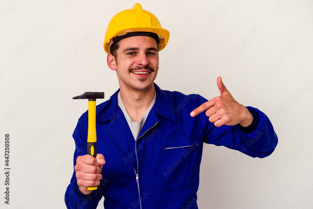 Young caucasian worker man holding a hammer isolated on white background person pointing by hand to a shirt copy space, proud and confident Young caucasian worker man holding a hammer isolated on white background person pointing by hand to a shirt copy space, proud and confident