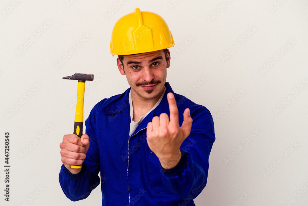 Young caucasian worker man holding a hammer isolated on white background pointing with finger at you as if inviting come closer.