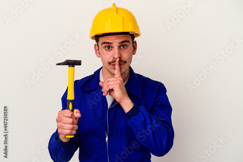 Young caucasian worker man holding a hammer isolated on white background keeping a secret or asking for silence.