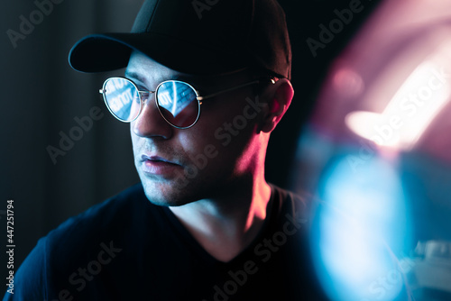 Neon light in glasses of a man. Futuristic cyber studio portrait. Techno glow and vibrant cyberpunk color. Male model with sunglasses in fluorescent illumination. Future mood. Urban fashion style.