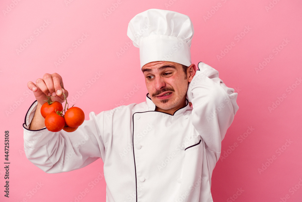 Young caucasian chef man holding tomatoes isolated on pink background touching back of head, thinking and making a choice. Young caucasian chef man holding tomatoes isolated on pink background touching back of head, thinking and making a choice.