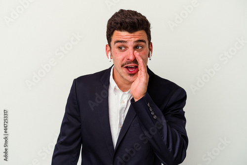 Young business caucasian man wearing wireless headphones isolated on white background is saying a secret hot braking news and looking aside