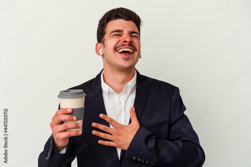 Young business caucasian man wearing wireless headphones and holding take way coffee isolated on white background laughs out loudly keeping hand on chest. Young business caucasian man wearing wireless headphones and holding take way coffee isolated on white background laughs out loudly keeping hand on chest.