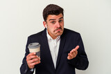 Young business caucasian man wearing wireless headphones and holding take way coffee isolated on white background shrugs shoulders and open eyes confused.