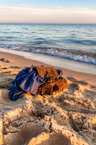 Travel and vacation concept. Empty sandy beach at sunset. Stylish brown backpack of traveler on seashore. Baltic Sea, Hel, Pomerania, Poland