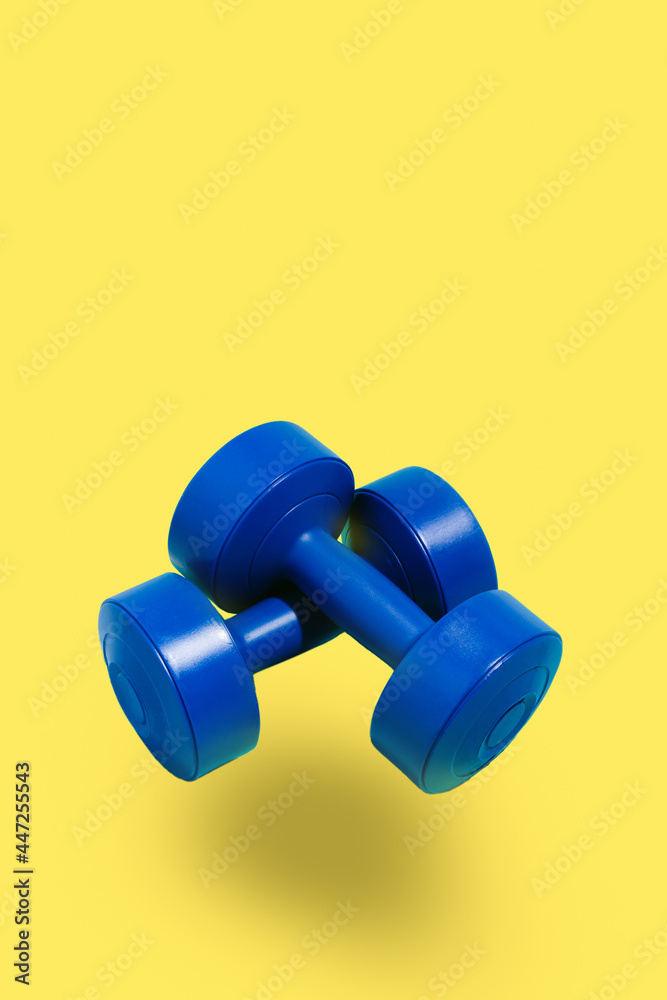 blue dumbbells on yellow background. Sport and exercise.