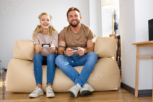 Great leisure time at home. Positive beloved couple sit playing video games at home, portrait of caucasian man and woman in casual outfit spending leisure time at weekends, have fun. copy space