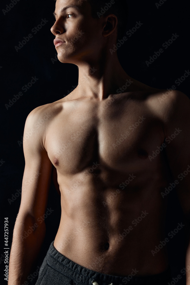 sexy bodybuilder with naked torso on black background looking to the side cropped view