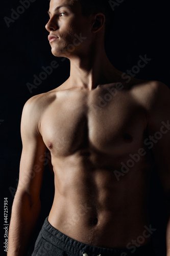 sexy bodybuilder with naked torso on black background looking to the side cropped view