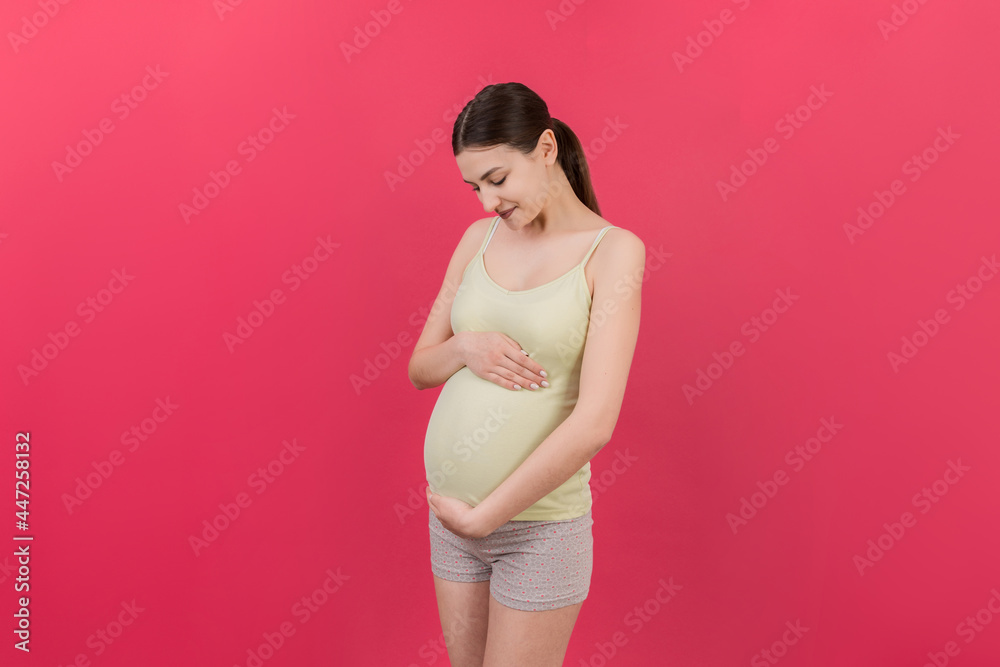 Happy pregnant woman touching her abdomen at Colored background. Future mother. Expecting of a baby. Copy space Happy pregnant woman touching her abdomen at Colored background. Future mother. Expecting of a baby. Copy space