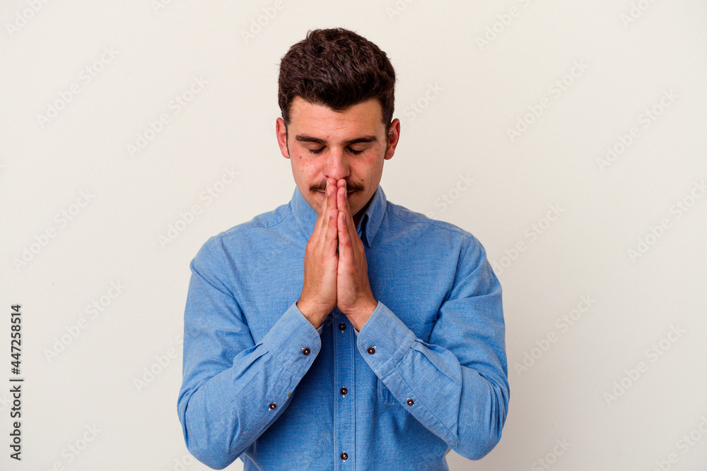 Young caucasian man isolated on white background praying, showing devotion, religious person looking for divine inspiration.