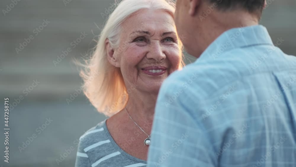 A happy elderly couple man and woman are talking to each other while walking outdoors A happy elderly couple man and woman are talking to each other while walking outdoors