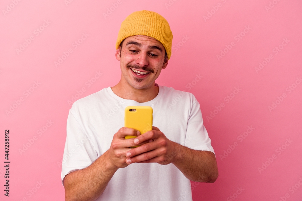 Young caucasian man holding a mobile phone isolated on pink background Young caucasian man holding a mobile phone isolated on pink background