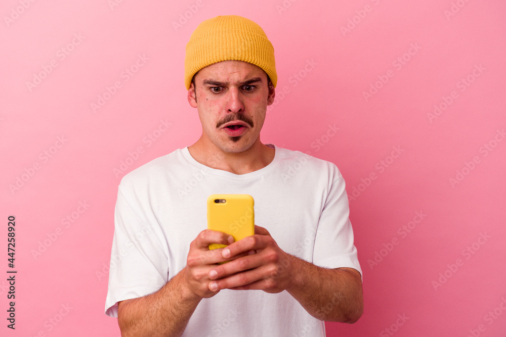 Young caucasian man holding a mobile phone isolated on pink background Young caucasian man holding a mobile phone isolated on pink background