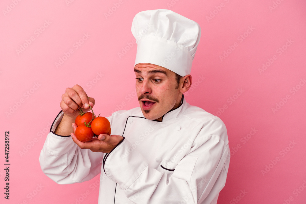 Young caucasian chef man holding tomatoes isolated on pink background