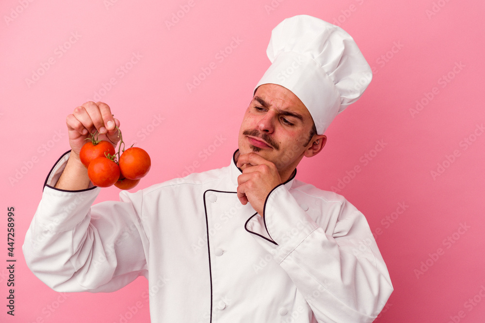 Young caucasian chef man holding tomatoes isolated on pink background Young caucasian chef man holding tomatoes isolated on pink background