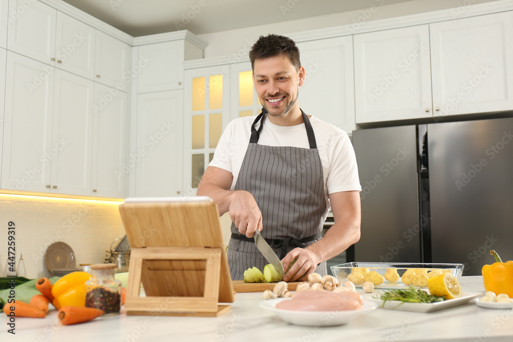 Happy man making dinner while watching online cooking course via tablet in kitchen Happy man making dinner while watching online cooking course via tablet in kitchen