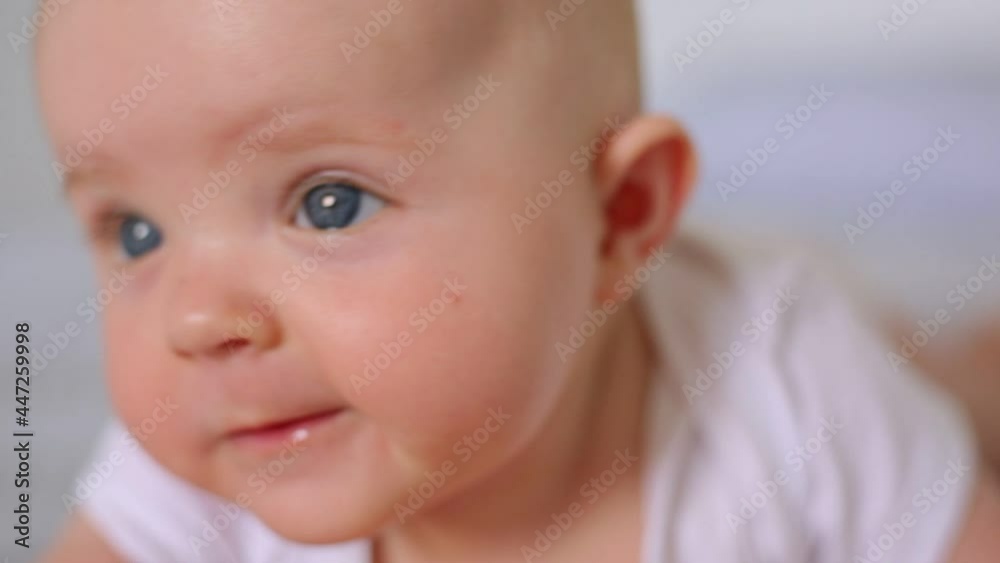 Close up of newborn little girl wearing white clothing playing, studying world around, smiling happily, having tummy time, infant developing, baby lying in bed on blanket. Close up of newborn little girl wearing white clothing playing, studying world around, smiling happily, having tummy time, infant developing, baby lying in bed on blanket.