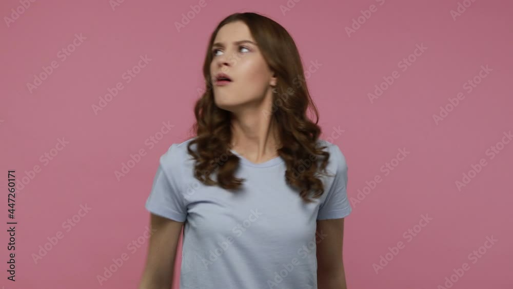 Serious bossy girl in casual blue T-shirt pointing finger at you looking at camera with confidence, controlling and demanding to do immediately. Indoor studio shot isolated over pink background.