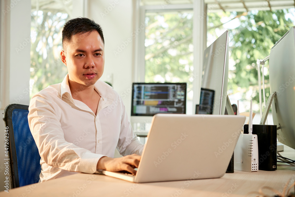 Serious frowning software developer working on laptop at his office desk Serious frowning software developer working on laptop at his office desk