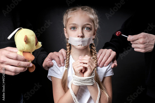 Child abuse. Abduction of children. Slavery and the sale of people. Psychological violence.Scared caucasian little girl is afraid of man in black, kidnapping her. Isolated on black studio background photo