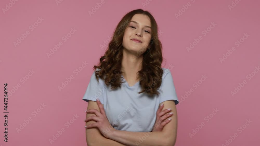 Cheerful attractive teenager girl with wavy hair in T-shirt turning half to camera and crossing hands, smiling friendly, looking confident and happy. Indoor studio shot isolated over pink background. Cheerful attractive teenager girl with wavy hair in T-shirt turning half to camera and crossing hands, smiling friendly, looking confident and happy. Indoor studio shot isolated over pink background.
