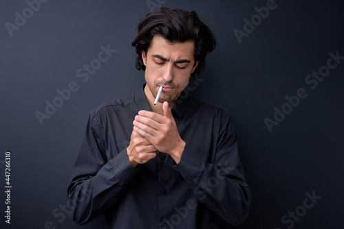 Handsome cool man with Cigarette, going to smoke, isolated on black background, copy space for advertisement. Portrait of brunette man in black shirt light cigarette. copy space. Smoking concept