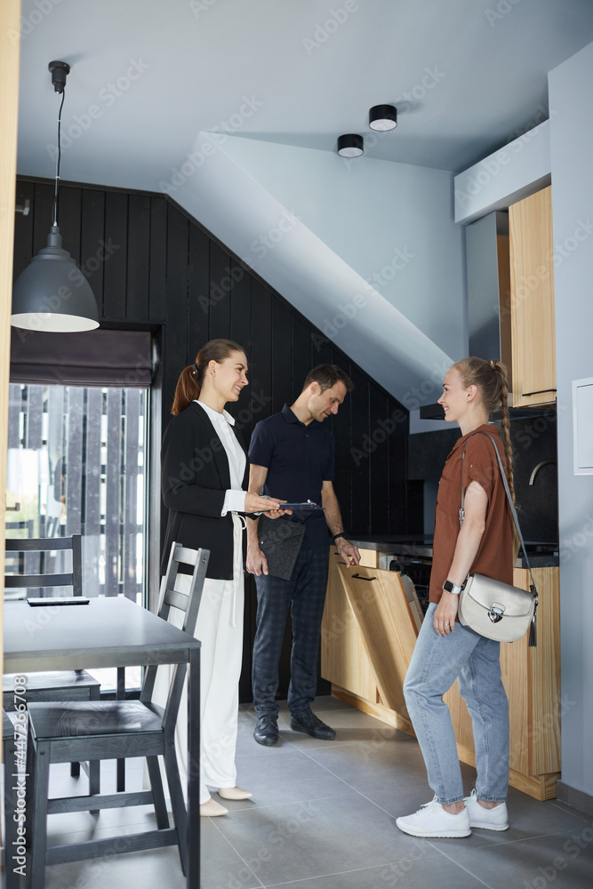Fototapeta premium Vertical full length portrait of smiling real estate agent showing house to young couple buying property