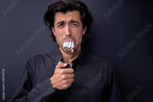 Funny portrait of crying frightened man with many cigarettes in mouth, quit smoking. Caucasian male has addiction. Studio shot isolated on black. Addiction concept. Copy space for advertisement.