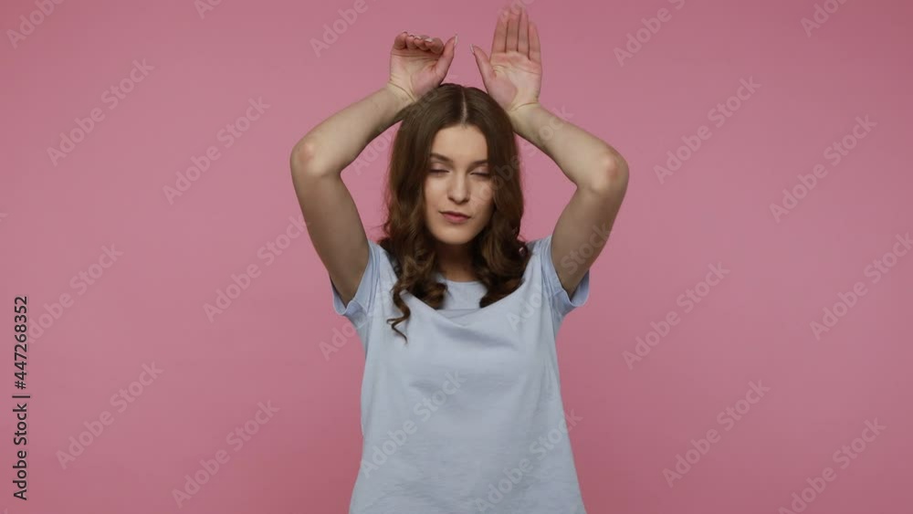 Funny adorable teenager with long black hair in T-shirt showing bunny ears with arms, rabbit gesture and having fun, looking cute childish. Indoor studio shot isolated over pink background. Funny adorable teenager with long black hair in T-shirt showing bunny ears with arms, rabbit gesture and having fun, looking cute childish. Indoor studio shot isolated over pink background.