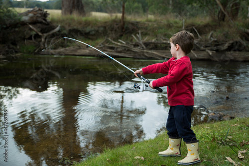 Side view of an adorable Australian little boy fishing bythe river in the woods photo