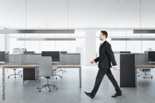 Businessman in suit walking in bright coworking meeting room interior with daylight, furniture and equipment. Design and ceo worker concept.