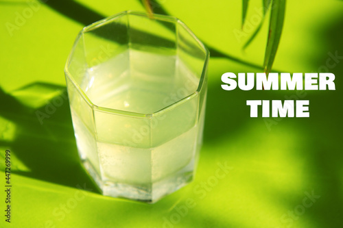 Glass of fresh cold water on a bright green background among green foliage with contrasting shadows from the bright sun. Summer time