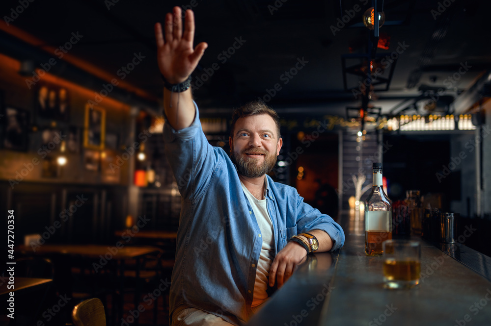 Bearded man with raised hand sitting in bar