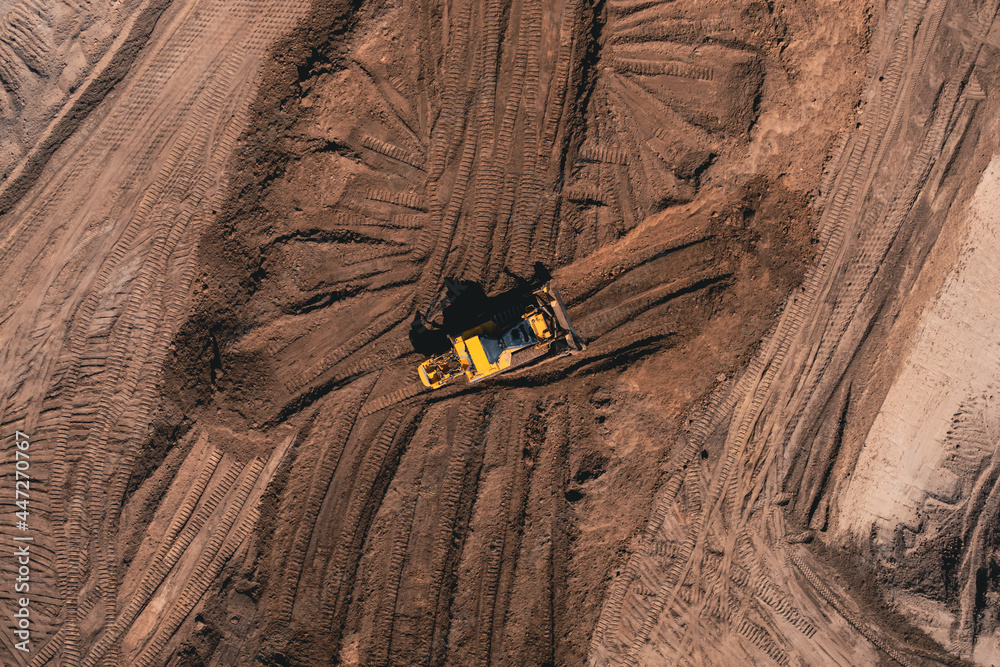Yellow Bulldozer carries out excavation work in a clay quarry - aerial drone top view. Crawler Bulldozer tears the ground apart with a bucket.