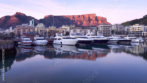Table Mountain sunrise is reflected in the still waters of a marina for luxury motor yachts in Cape Town, South Africa