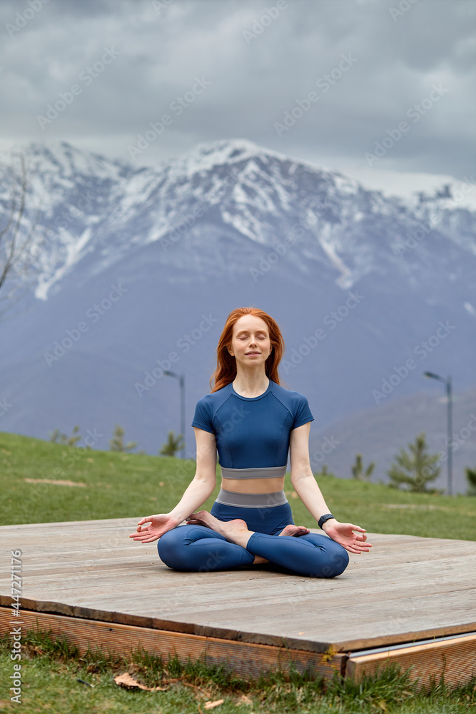 Adorable young woman sitting outdoors in yoga position and meditating with closed eyes in nature. Peaceful female enjoy rest, relax in tranquility. side view portrait