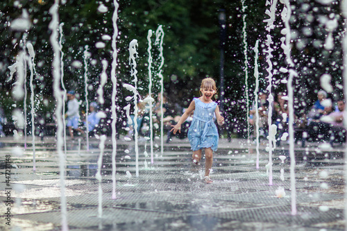 happy little girl running under splashing water