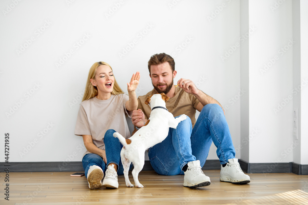 Happy caucasian couple family sit on floor playing with pet dog, have fun, enjoy weekends together, laugh, in casual outfit, talking. Harmonious relationships, family, spare time, free time concept Happy caucasian couple family sit on floor playing with pet dog, have fun, enjoy weekends together, laugh, in casual outfit, talking. Harmonious relationships, family, spare time, free time concept